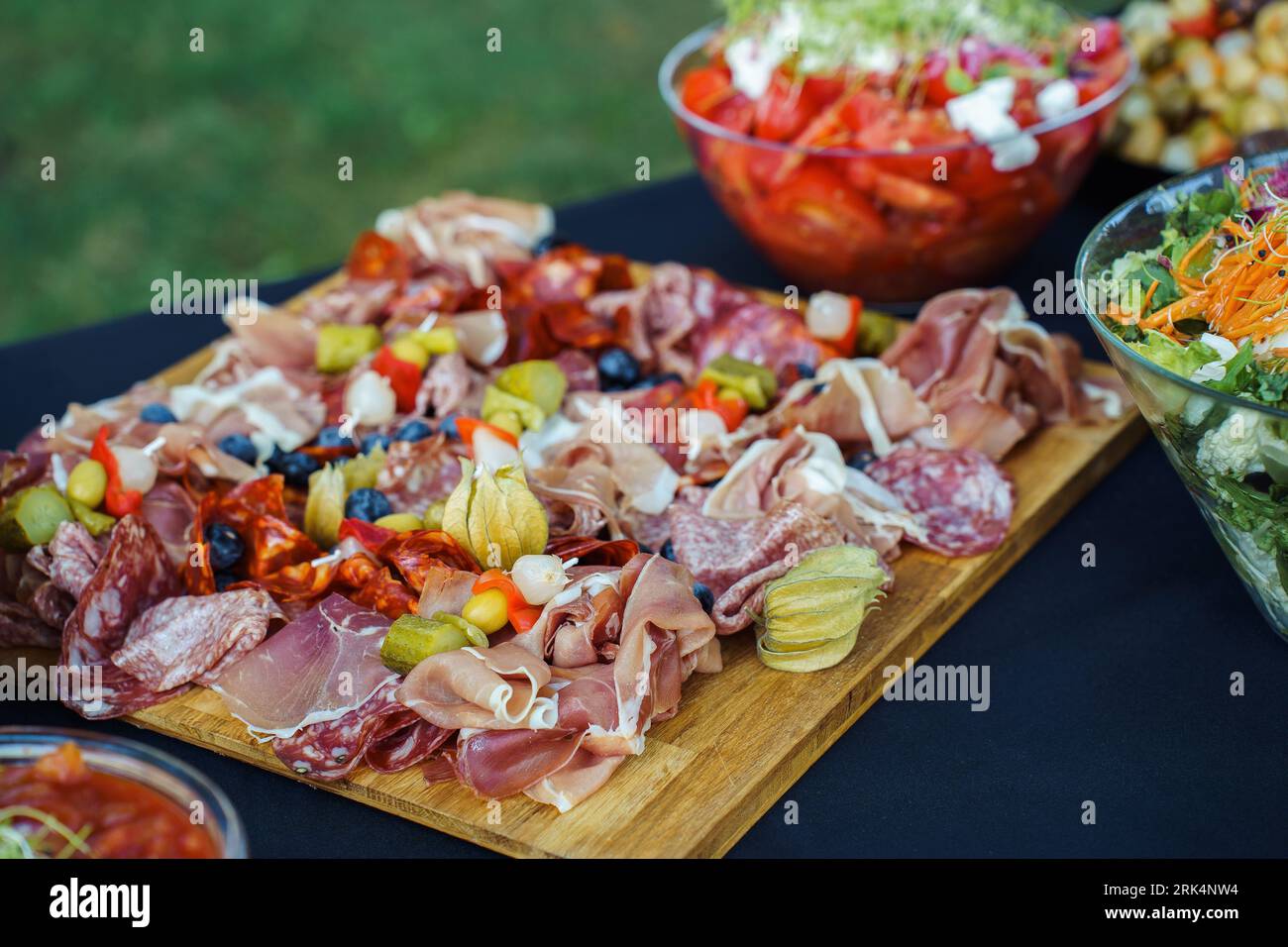 Tavola di legno con salumi a fette, olive e physalis, oltre ad altri spuntini sul tavolo durante il buffet in giardino Foto Stock