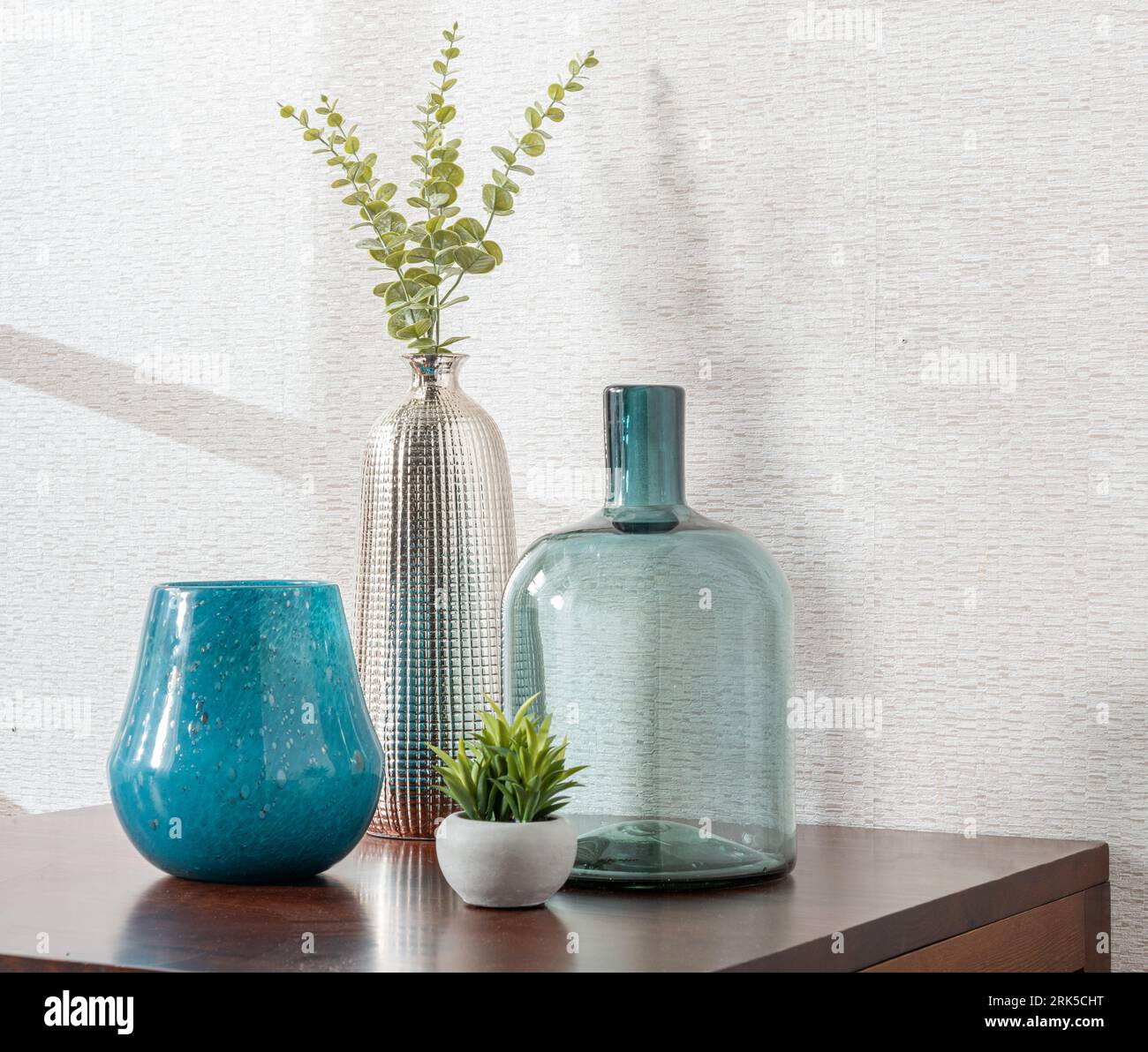 Un ambiente interno caratterizzato da diversi vasi decorati e vegetazione lussureggiante collocata sopra un tavolo di legno Foto Stock