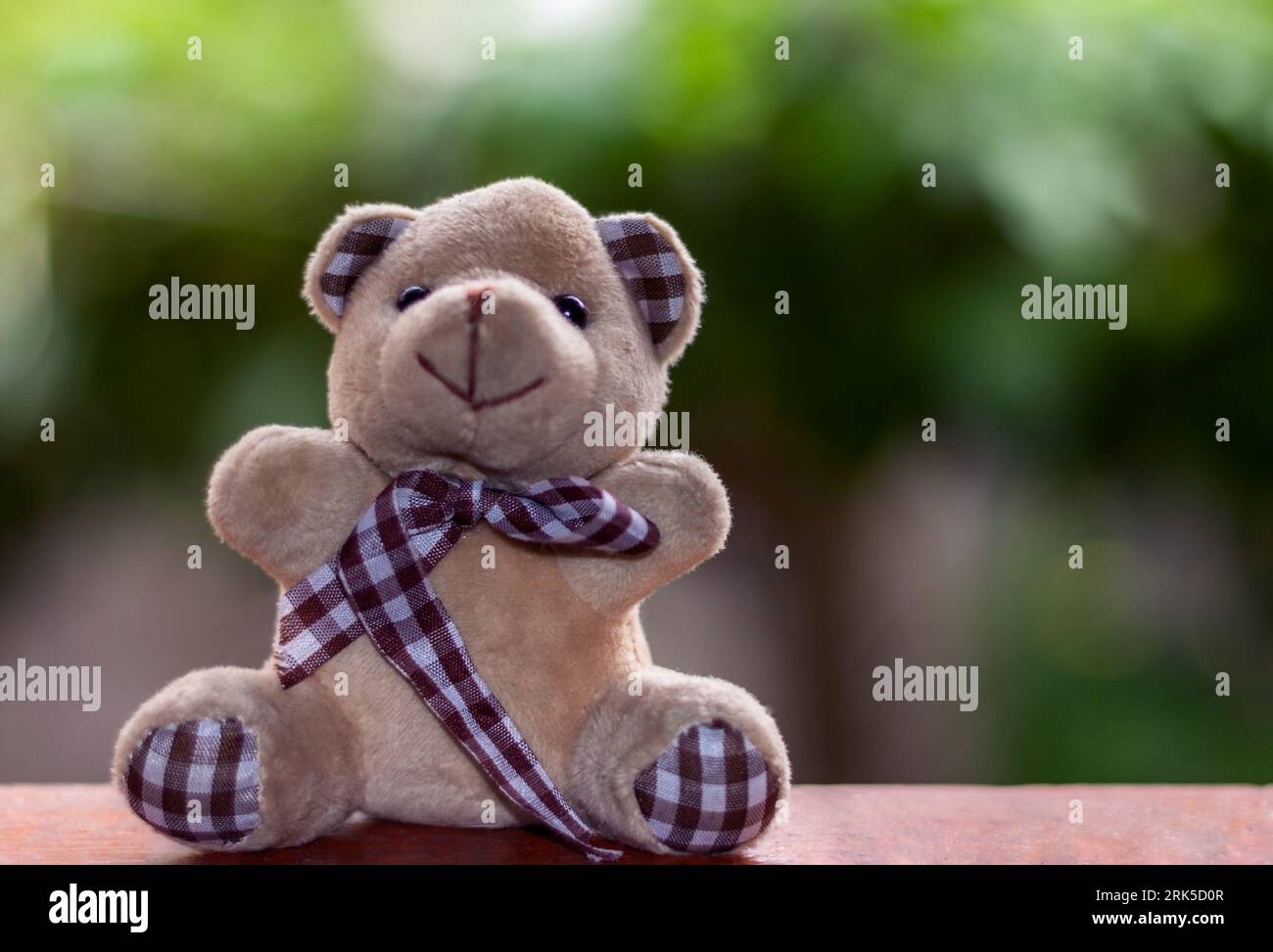 Un grazioso orsacchiotto marrone imbottito si trova sopra un tavolo di legno con un nastro luminoso Foto Stock