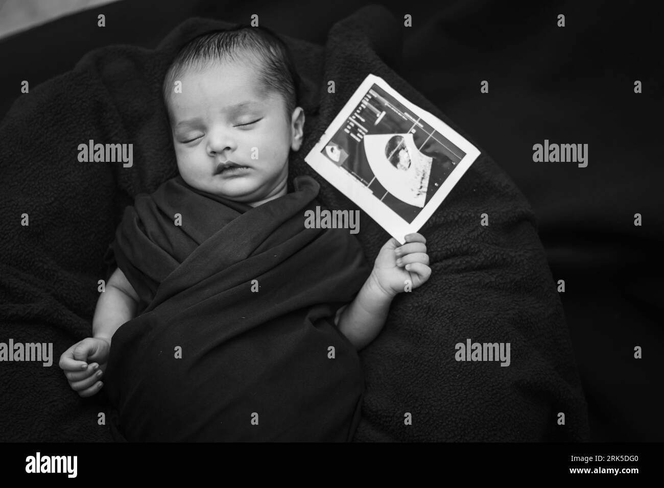 neonato che tiene in mano una copia ecografica e dorme al palmo della madre in bianco e nero Foto Stock