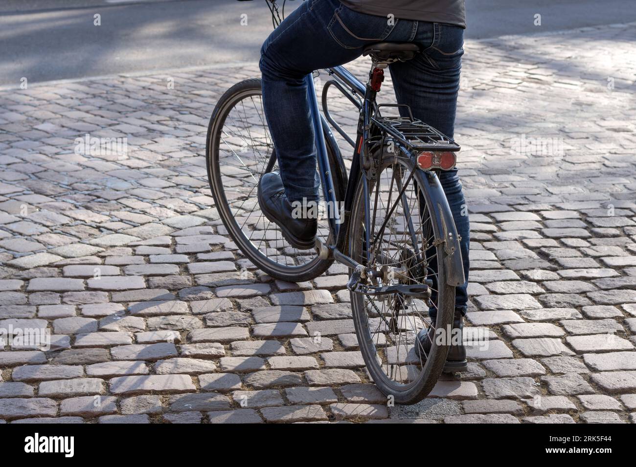 un uomo con una bici nera da città si erge su ciottoli Foto Stock