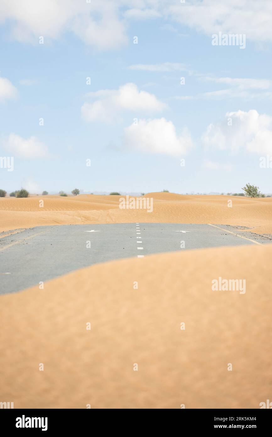 (Attenzione selettiva) splendida vista di una strada deserta coperta da dune di sabbia. Strada vuota che attraversa il deserto di Dubai. Dubai, Emirati Arabi Uniti. Foto Stock