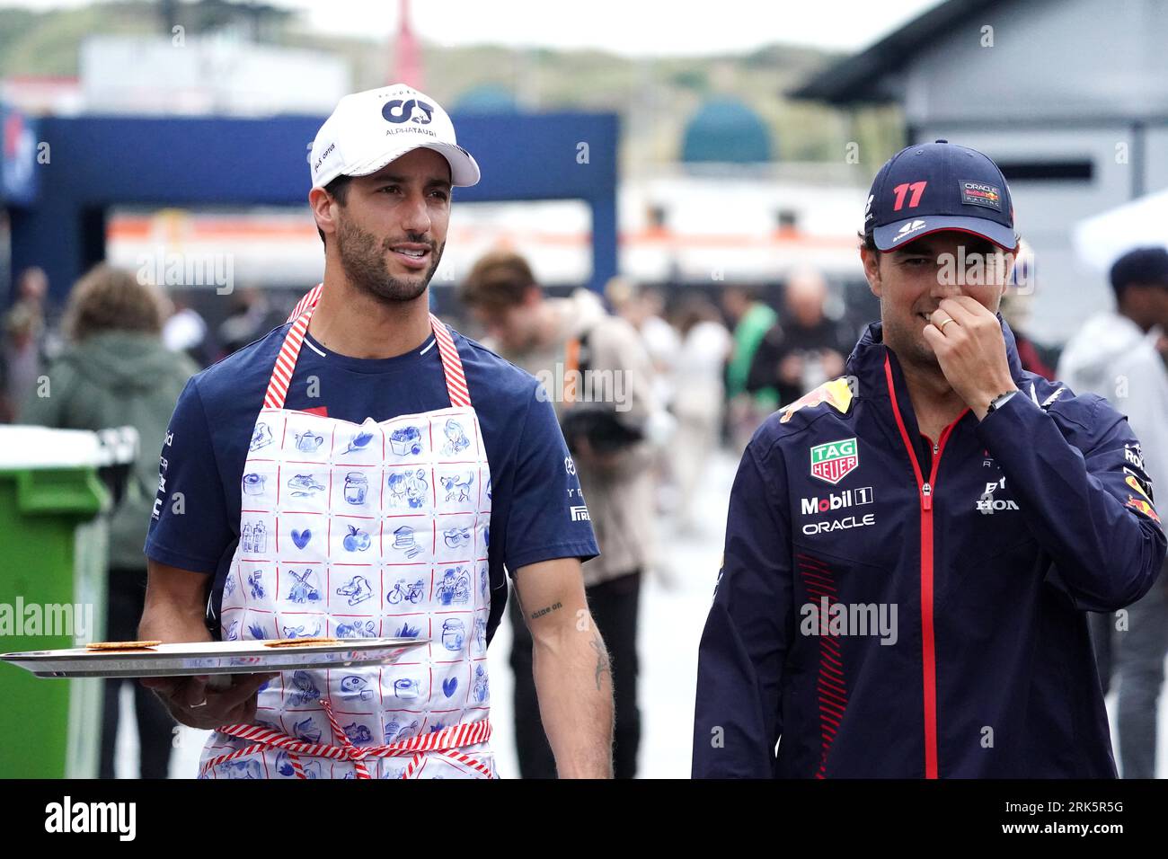 AlphaTauri pilota di F1 Daniel Ricciardo (a sinistra) con Sergio Perez pilota di F1 Red Bull Racing che detiene un piatto di Stroopwafel durante una giornata di anteprima in vista del Gran Premio di Olanda 2023 di domenica sul circuito Zandvoort CM.com a Zandvoort, Paesi Bassi. Data foto: Giovedì 24 agosto 2023. Foto Stock