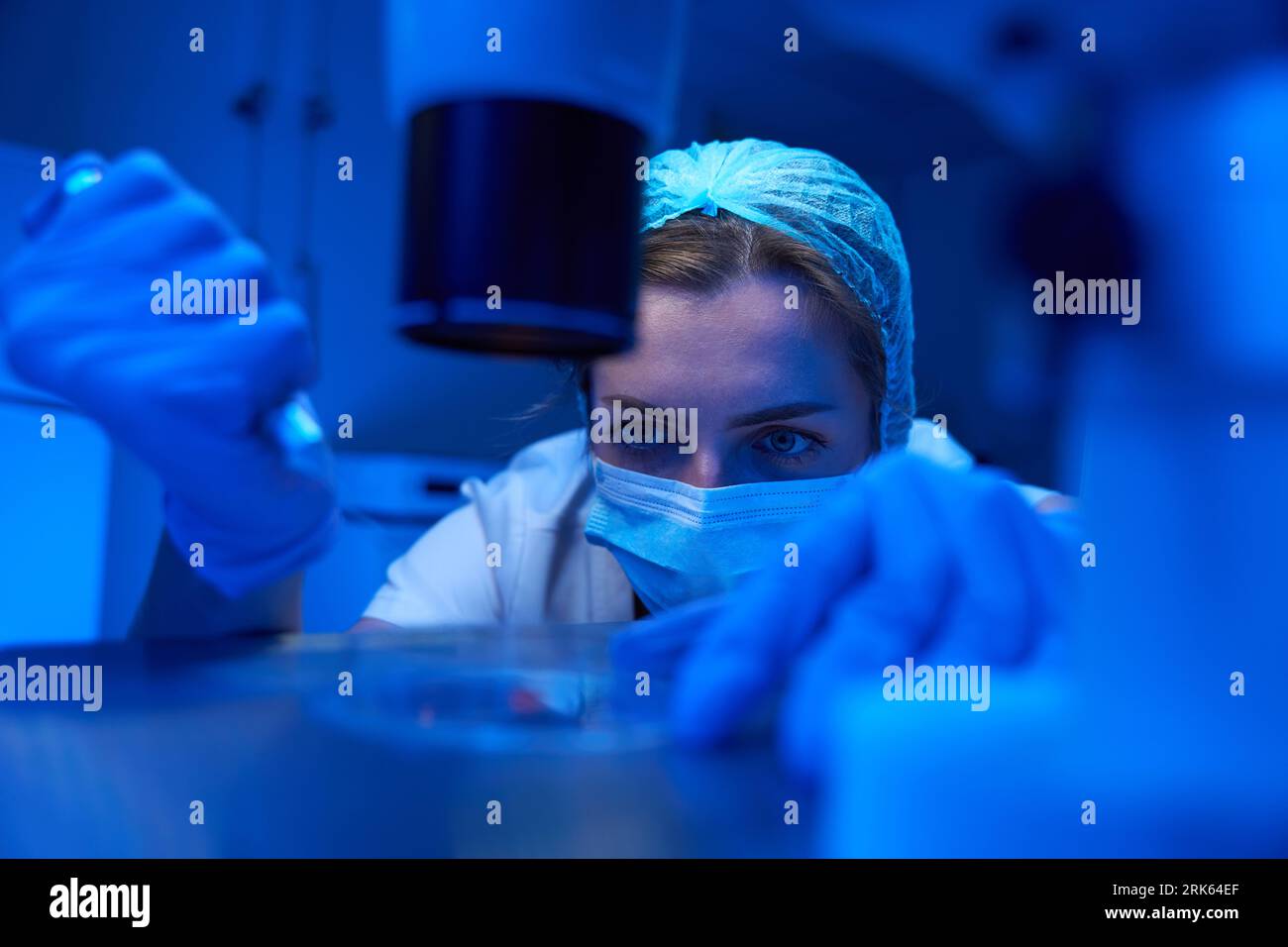 Donna in maschera protettiva lavora con biomateriale in laboratorio sterile Foto Stock
