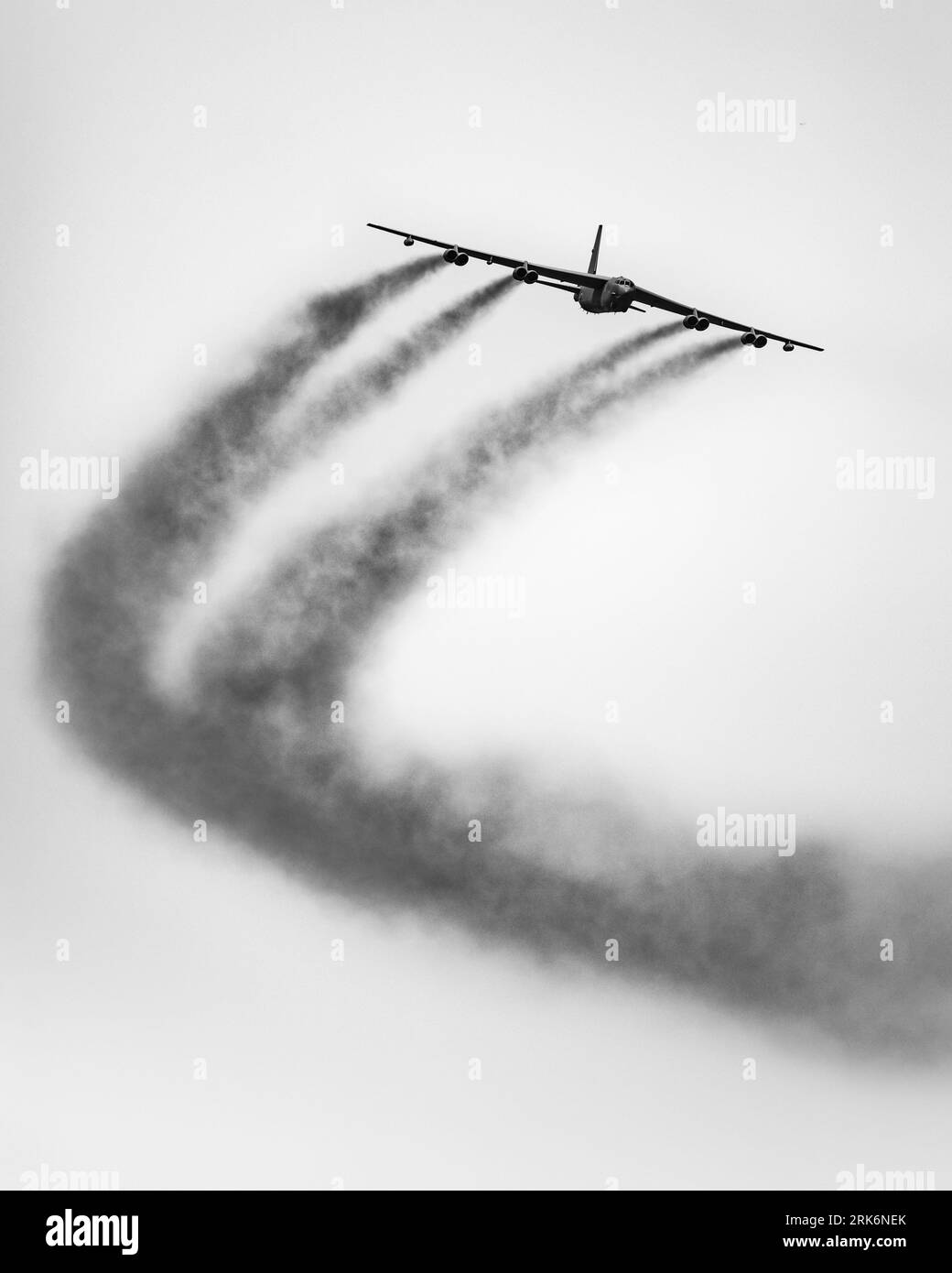 Un colpo verticale in scala di grigi di un aereo commerciale che vola lasciando fumo Foto Stock