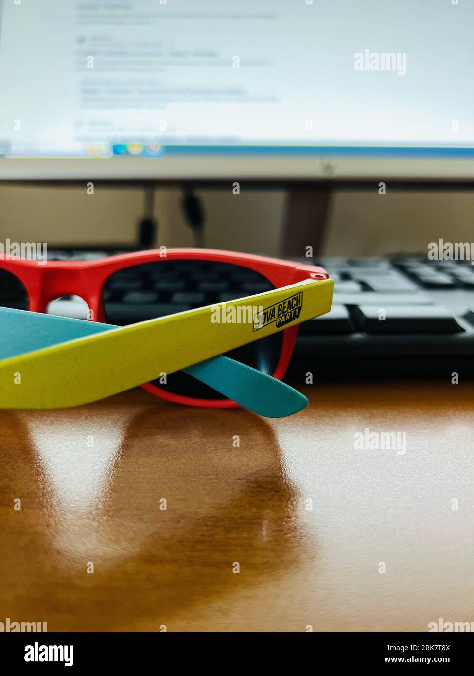 Un ambiente di lavoro contemporaneo con una scrivania per computer con un computer portatile e un paio di occhiali da sole Foto Stock