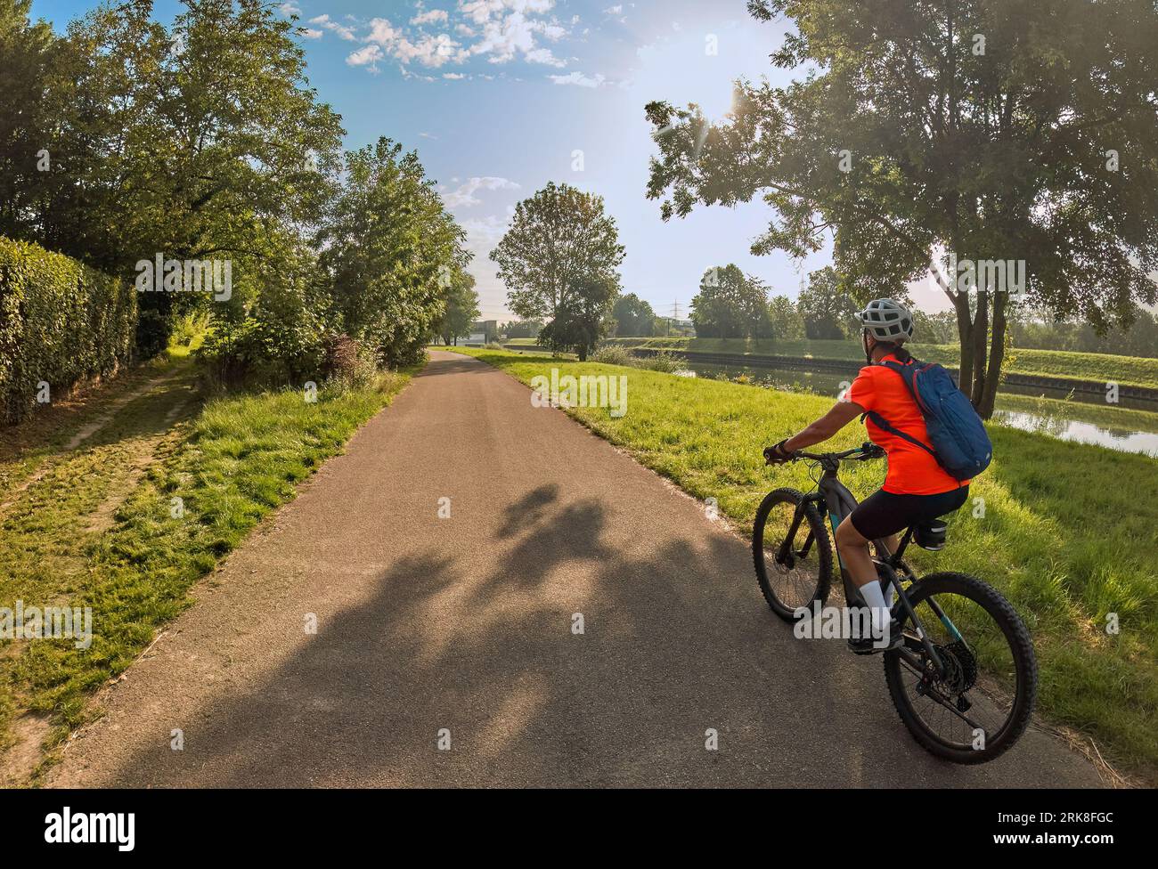 Donna simpatica con mountain bike elettrica, pedalando alla luce del mattino sulla pista ciclabile della valle del Neckar vicino Ludwigsburg, Baden Württemberg, Germania Foto Stock