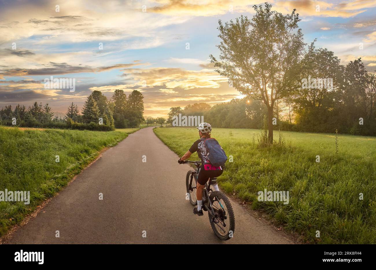 Donna simpatica con mountain bike elettrica, pedalando alla luce del mattino sulla pista ciclabile della valle del Neckar vicino Ludwigsburg, Baden Württemberg, Germania Foto Stock