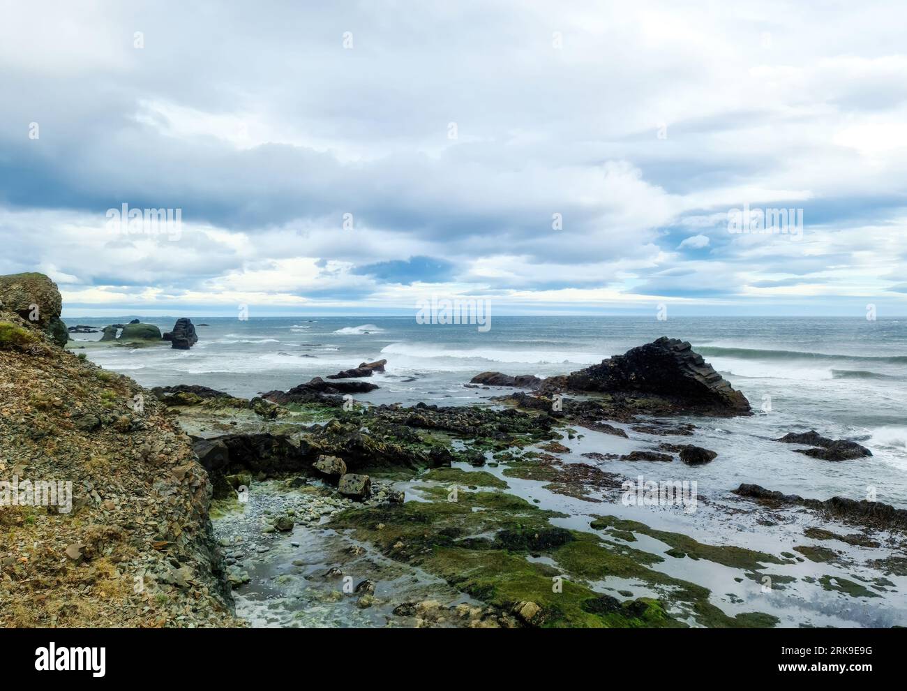 Una Rocky Beach con Bergs sull'Islanda con forti venti e potenti surfisti Foto Stock