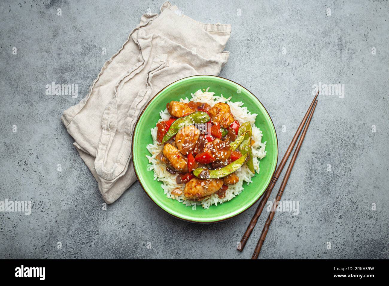 Pollo asiatico dolce e acaro appiccicoso con verdure saltate e riso in ciotola di ceramica con vista dall'alto chopsticks, sfondo grigio pietra rustica Foto Stock