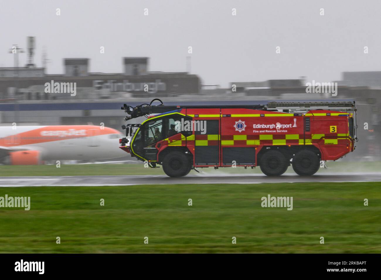 Un camion dei vigili del fuoco Rosenbauer Panther dell'aeroporto di Edimburgo scende lungo Una pista bagnata da pioggia durante un incidente di emergenza con Un A350 della Qatar Airways Foto Stock