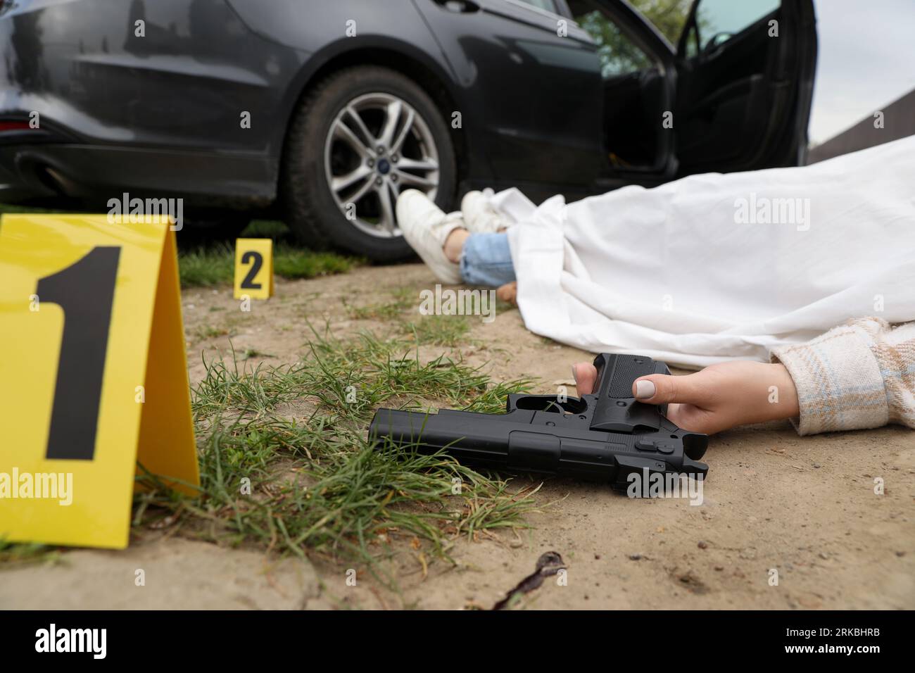 Scena del crimine con il corpo di una donna morta, pistola e marcatori all'aperto, primo piano Foto Stock