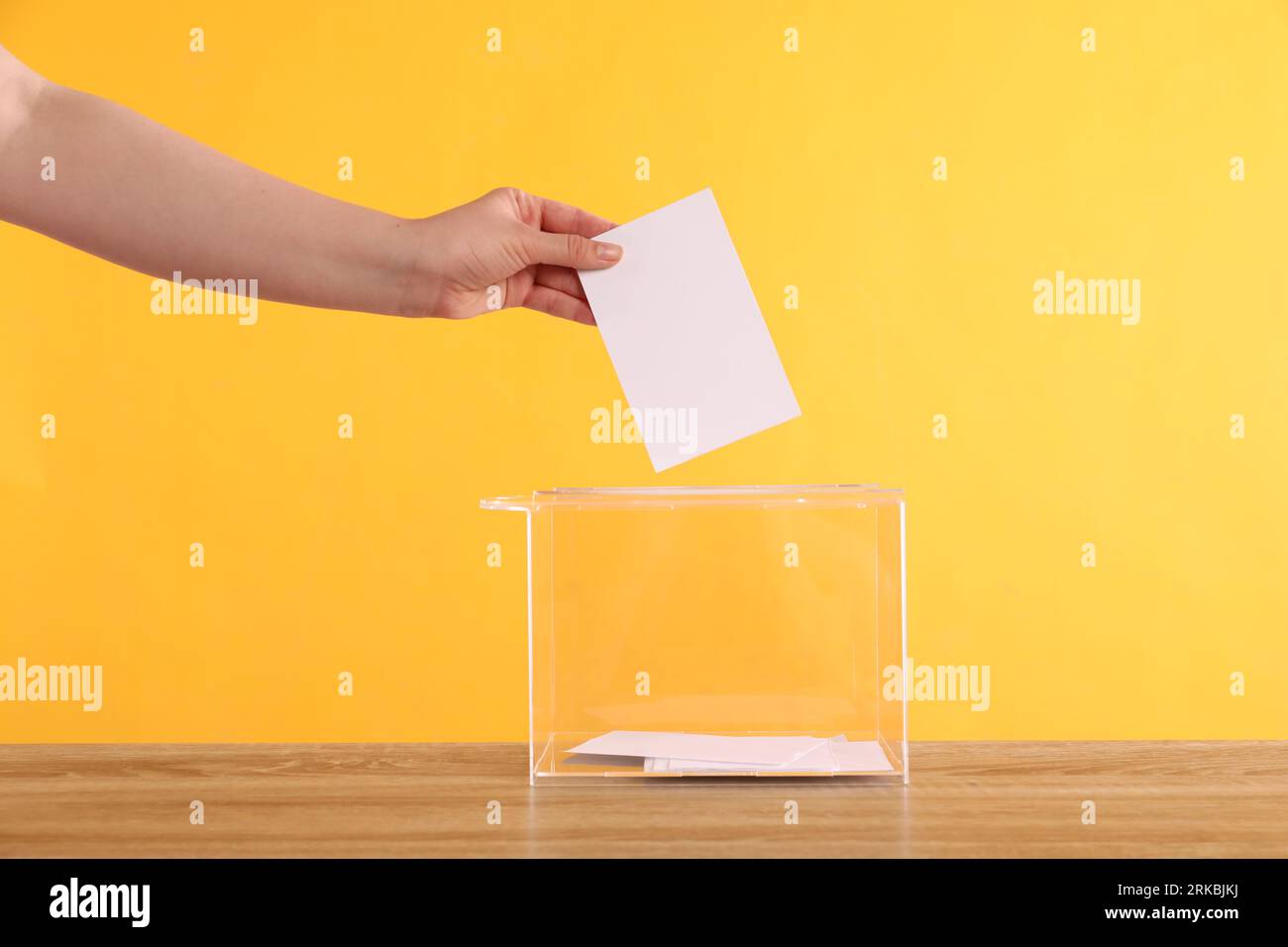 Donna che mette il suo voto nelle urne su un tavolo di legno su sfondo arancione, primo piano Foto Stock