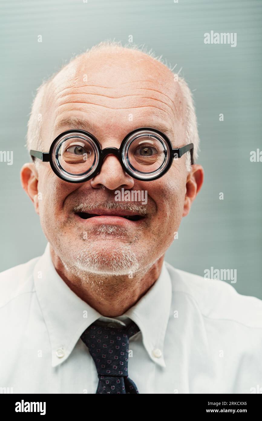 Signore più anziano, look sciocco, occhiali ultra-spessi, personifica umoristicamente un personaggio socialmente impegnativo ma meritevole. Ambiente formale, shir bianco Foto Stock