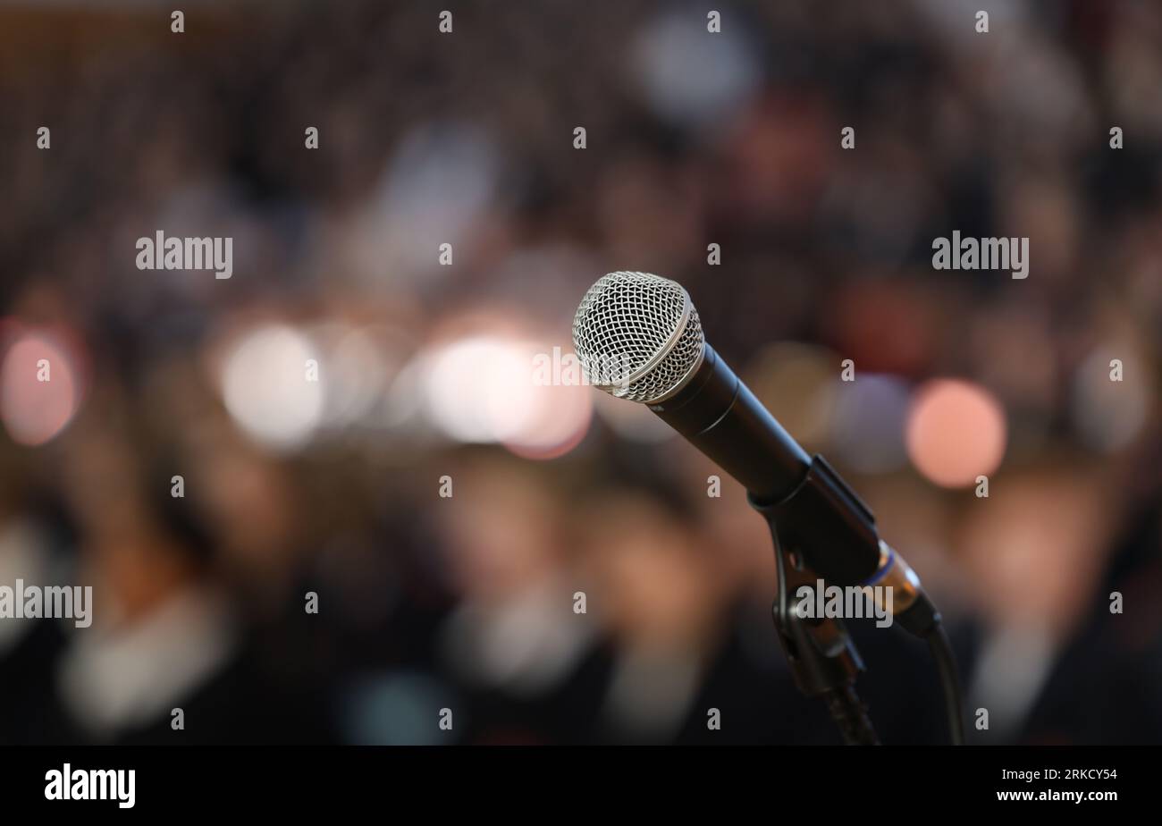 Primo piano di un microfono sul palco con un pubblico bokeh o una folla furiata. Parlare in pubblico con un tema nervoso o ansioso Foto Stock