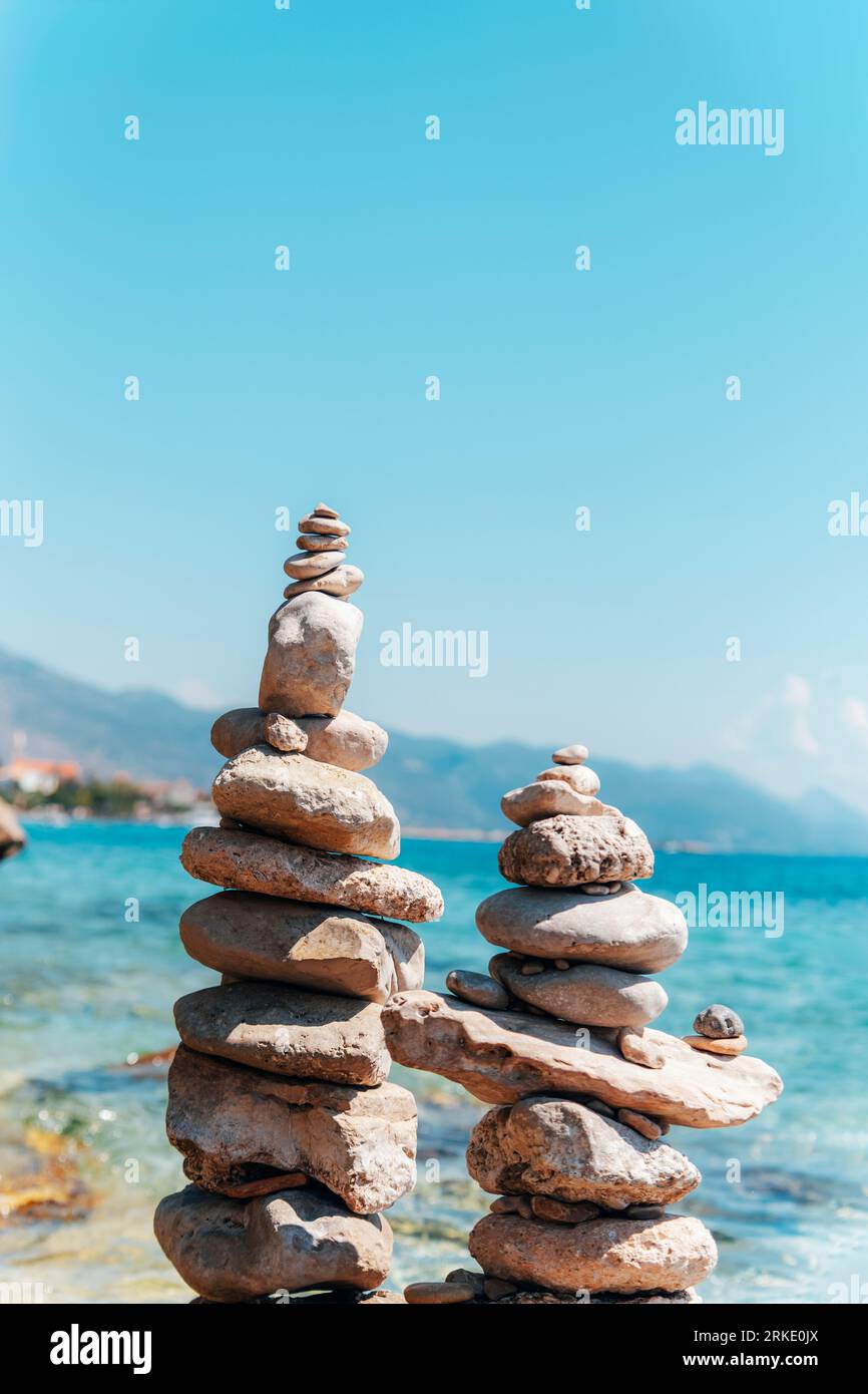 Le pietre piramidali si bilanciano sulla spiaggia sullo sfondo della costa blu del mare, primo piano. Foto Stock