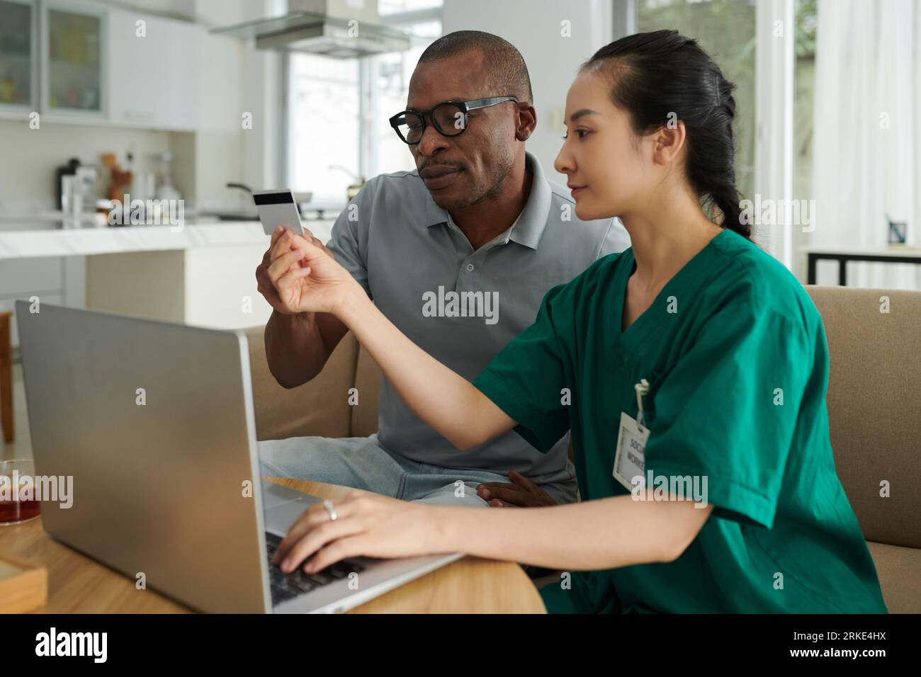 Assistente sociale che aiuta il paziente a inserire informazioni dalla carta di credito in forma online Foto Stock
