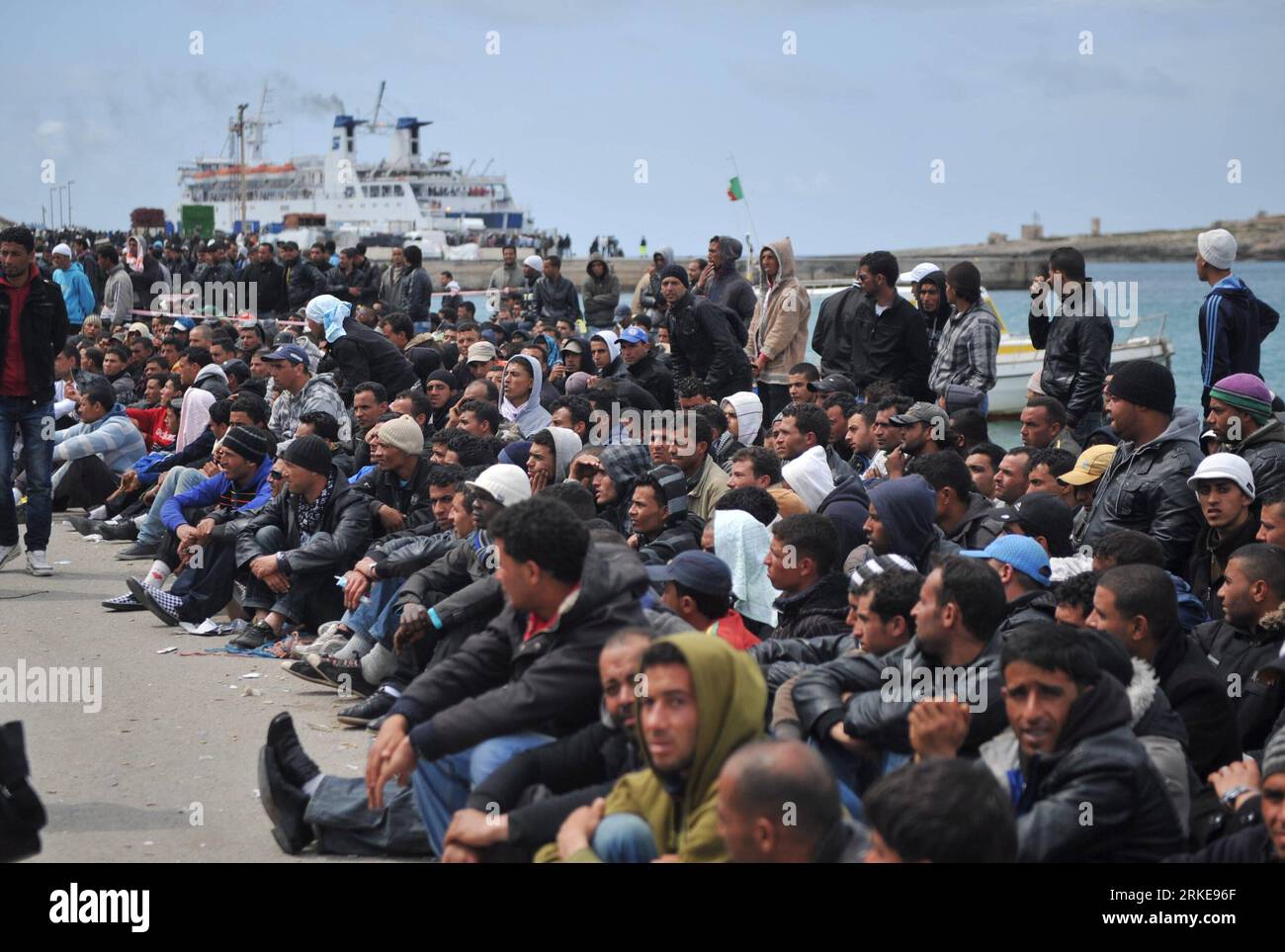 (110330) -- LAMPEDUSA, 30 marzo 2011 (Xinhua) -- gli immigrati clandestini dal Nord Africa aspettano il trasferimento al porto dell'isola di Lampedusa, Italia meridionale, 29 marzo 2011. Circa 18.000 immigrati nordafricani, principalmente dalla Libia e dalla Tunisia devastate dai disordini, hanno inondato la piccola isola italiana di Lampedusa, che si trova a soli 110 km dall'Africa. Ci si aspetta che più immigrati sbarchino qui con l'aggravarsi della crisi libica. A partire da mercoledì, l'Italia invierà altre navi con una capacità totale di 10.000 ormeggi per evacuare i migranti a Lampedusa. (Xinhua/Wang qingqin) (yc) ITALIA-LAMPEDUSA-NORD AF Foto Stock