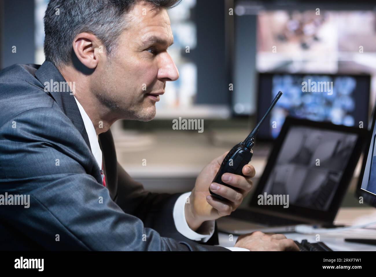 Imprenditore parlando su walkie talkie mentre guardano la telecamera TVCC riprese su più sullo schermo del computer Foto Stock