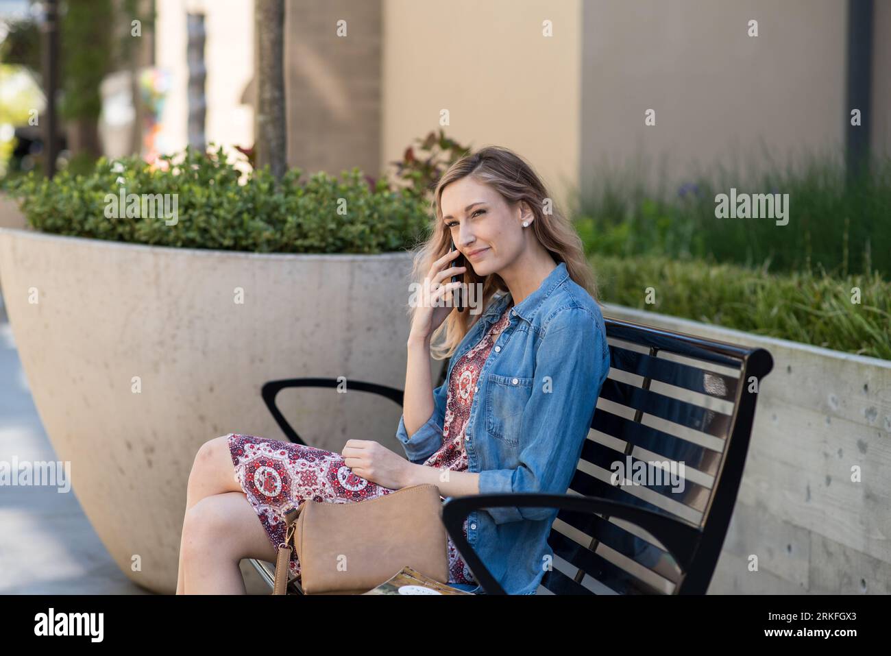 Giovane donna seduta sulla panchina che parla al telefono Foto Stock