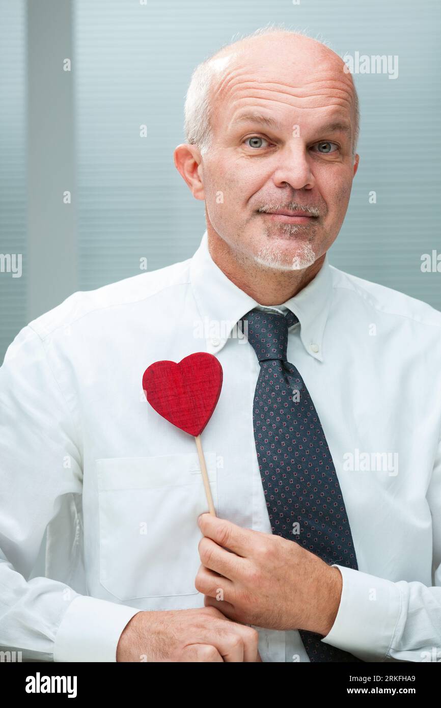 Uomo anziano in camicia bianca e cravatta che esprime amore, desiderando una famiglia, e ammirando attributi sia fisici che intellettuali, tenendo un lui simbolico Foto Stock