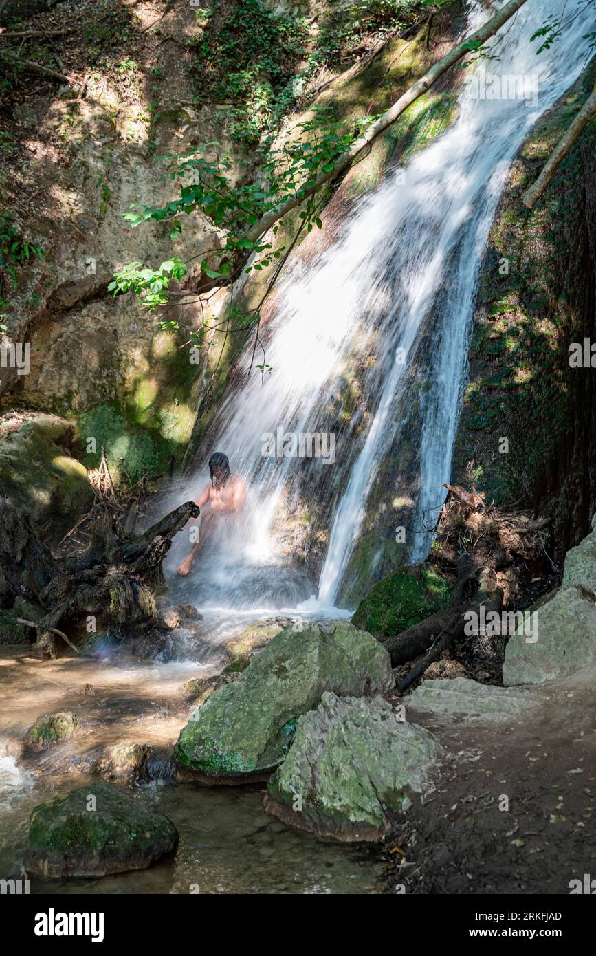 Un uomo sotto una cascata nel bosco. Foto Stock