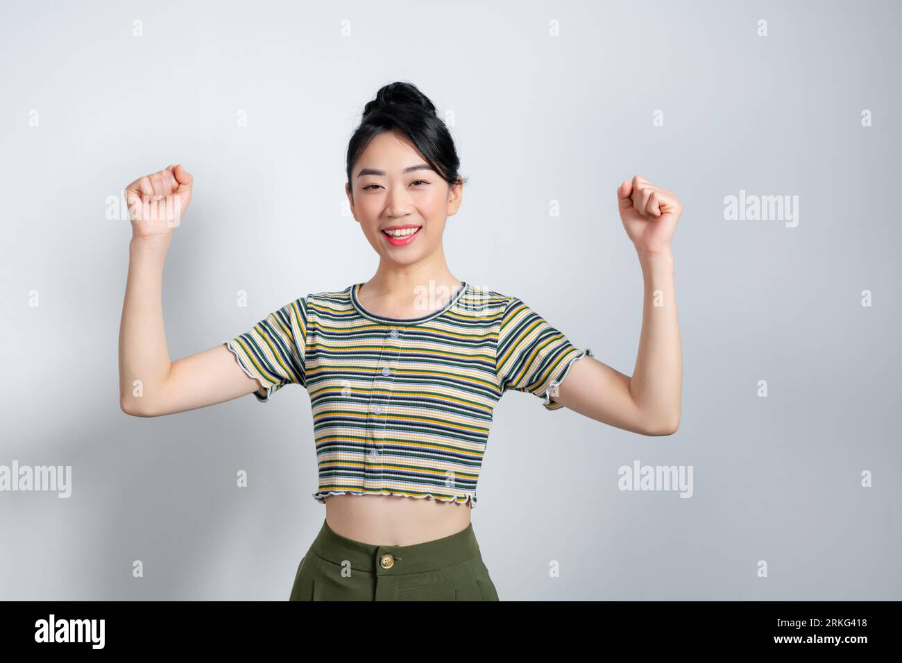 La bella donna asiatica solleva armi e pugni legati a festeggiare la vittoria che esprime il successo. Foto Stock