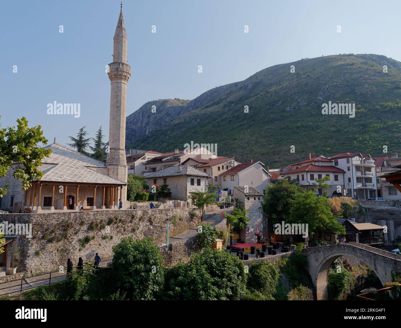 L'esterno della moschea Hadži Kurt è circondato da case e montagne e da un ponte sul fiume Nervetva, Mostar, Bosnia ed Erzegovina, 21 agosto 2023. Foto Stock