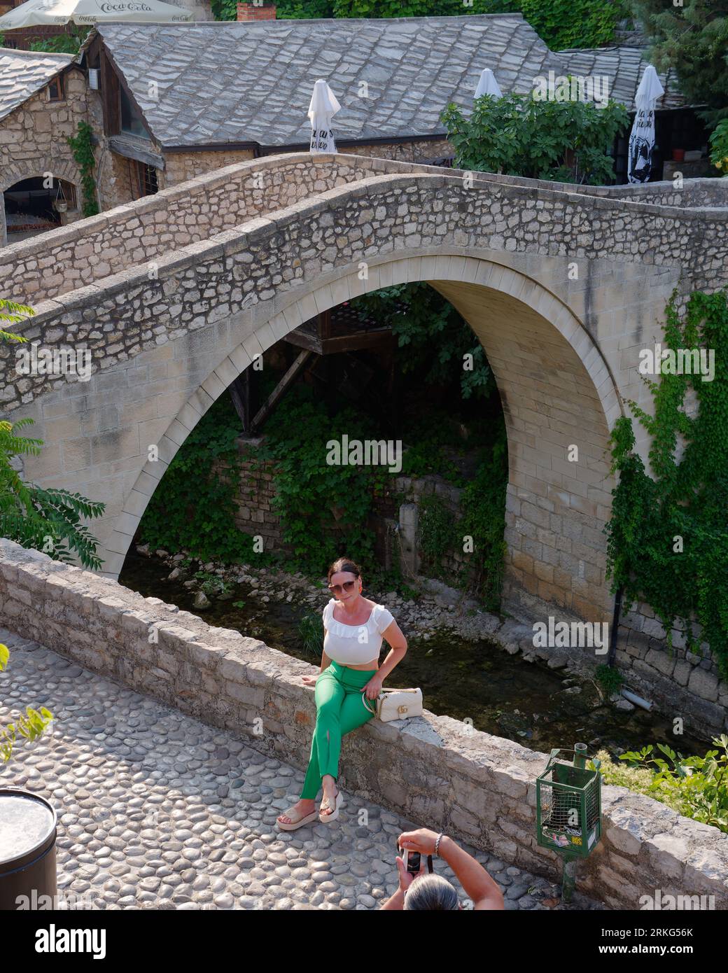 Donna siede su un muro accanto a un piccolo ponte su un'insenatura del fiume Neretva nella città di Mostar, Bosnia ed Erzegovina, 21 agosto 2023. Foto Stock