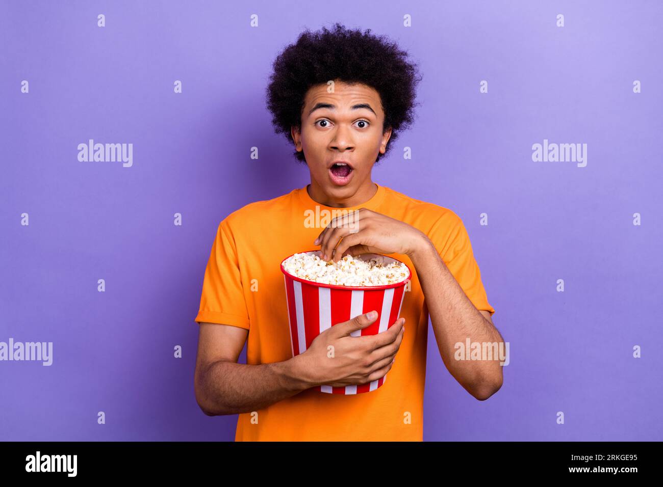 Foto di scioccata e divertente giovanile emozioni a bocca aperta sorpreso Hold bucket intrigo popcorn film DC isolato su sfondo di colore viola Foto Stock