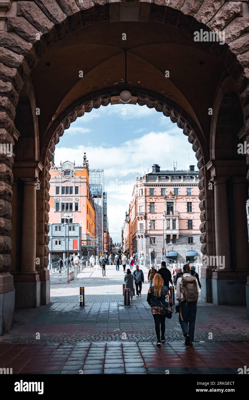 Un gruppo eterogeneo di individui che attraversano un imponente arco urbano a Stoccolma, Svezia Foto Stock