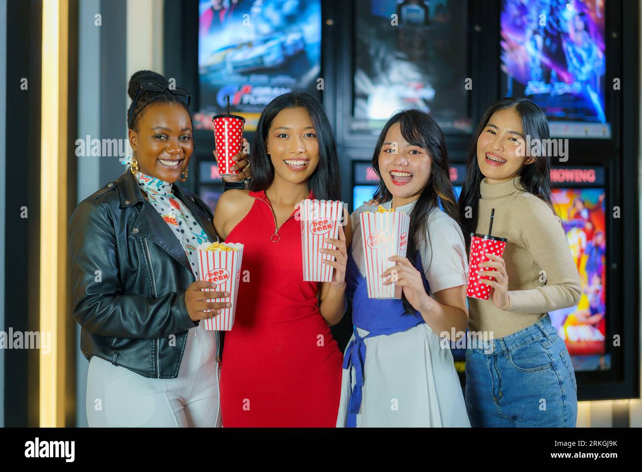 Amici diversi, popcorn in mano, passeggiate gioiosamente davanti al cinema, incarnando l'amicizia e l'attesa piena di divertimento per un film divertente Foto Stock