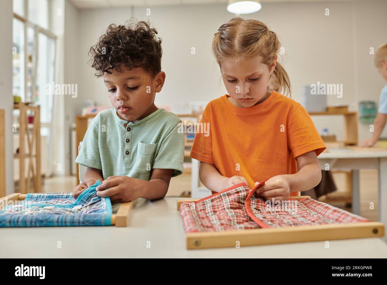 bambini multietnici che abbottonano stoffa su cornici in classe alla scuola montessori Foto Stock