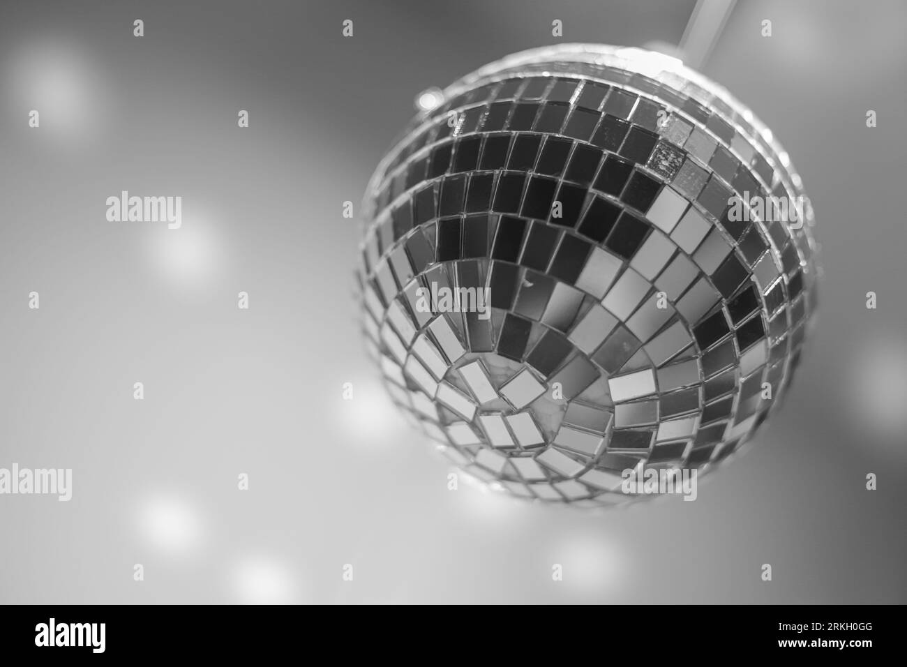 Una scintillante sfera da discoteca appesa a testa in giù dal soffitto, illuminando la stanza in scala di grigi Foto Stock