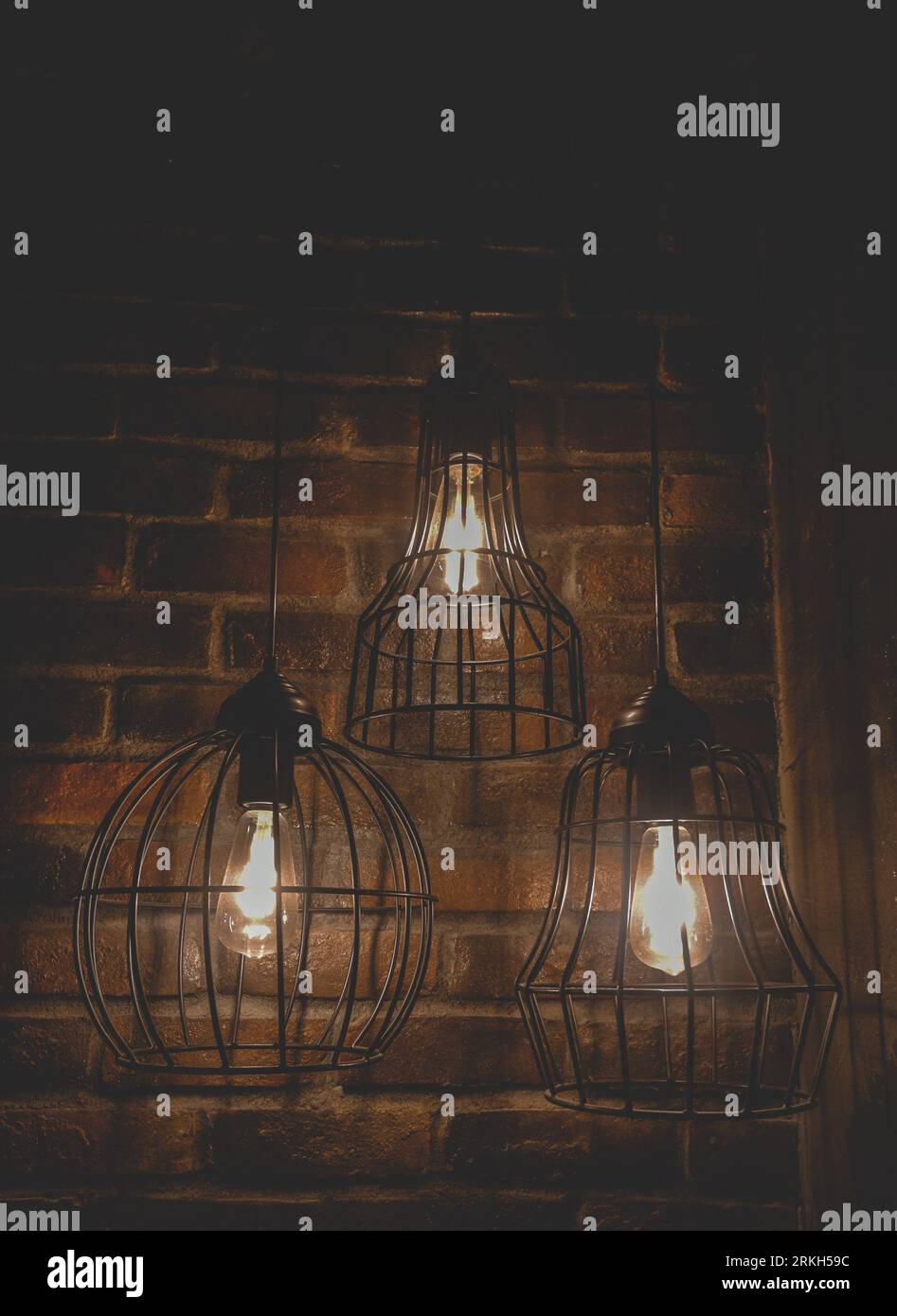 Un primo piano di tre moderne lampade in stile loft su uno sfondo di mattoni scuri Foto Stock