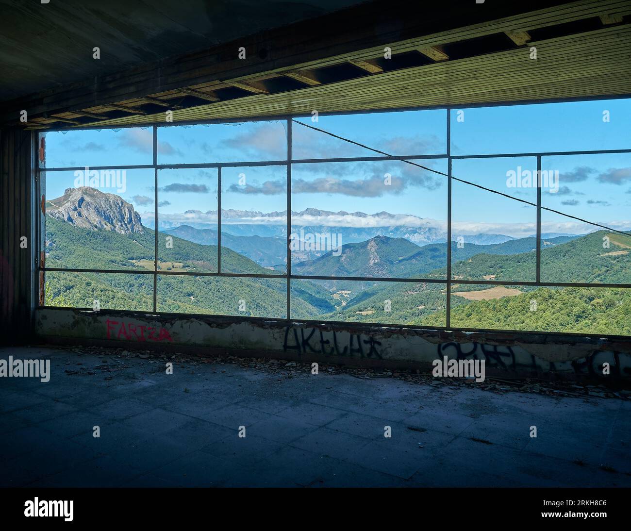 paesaggio montano visto attraverso una finestra, edificio in rovina con una finestra senza vetro che si affaccia su una valle di montagna con alte cime e nuvole Foto Stock