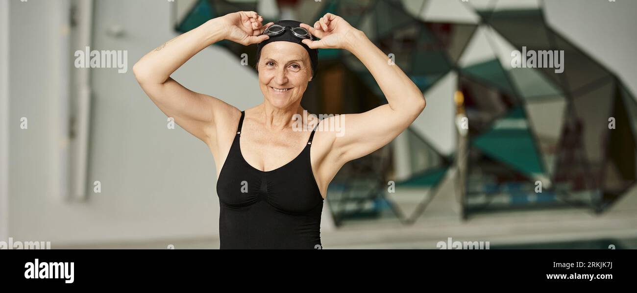 allegro nuotatore maturo con occhiali regolabili in costume da bagno, donna in berretto da bagno, centro benessere, banner Foto Stock