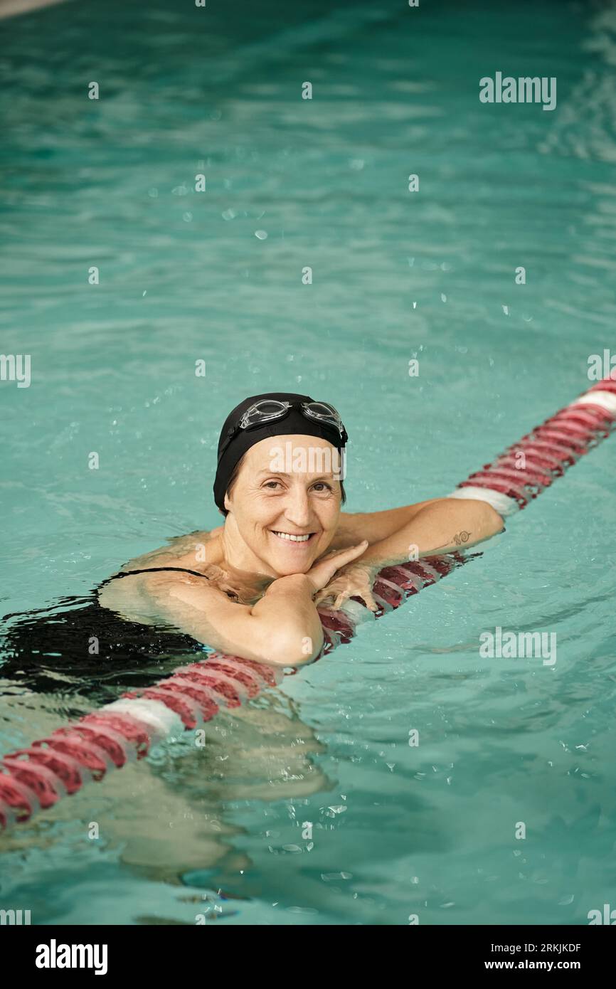 positivo donna di mezza età che nuota in piscina, sorriso, cuffia da bagno e occhiali, stile di vita sano, sport Foto Stock