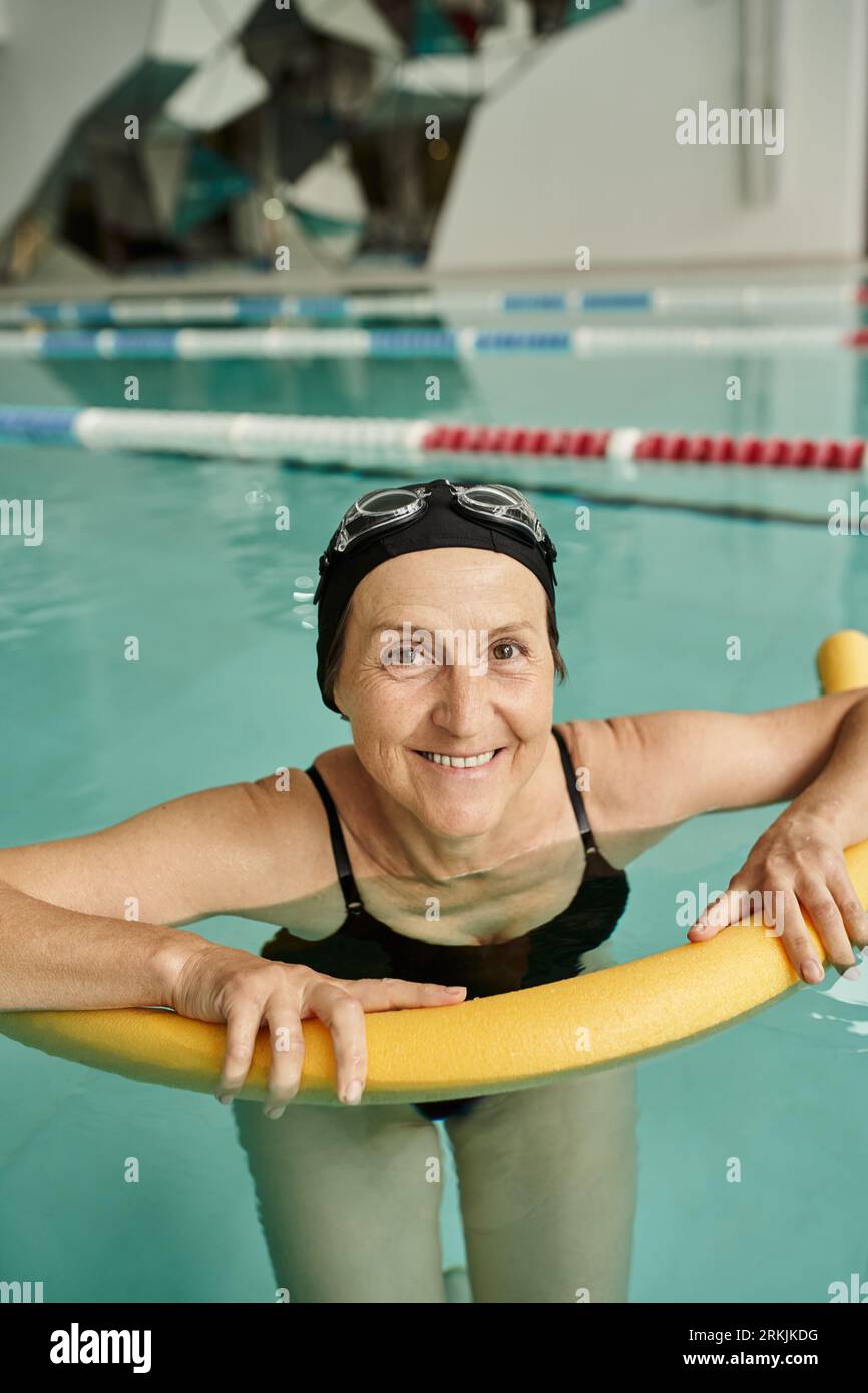 felice donna di mezza età che nuota con spaghetti da piscina, cuffia e occhiali, stile di vita sano, sport Foto Stock
