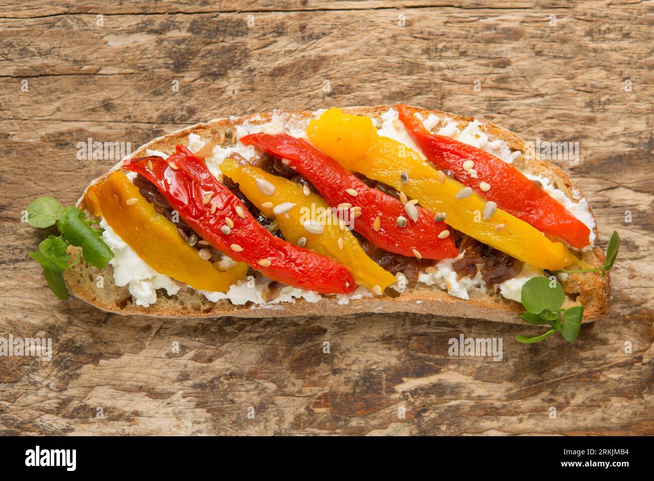 Un esempio di bruschetta fatta con pane tostato a pasta madre, ricotta, cipolle rosse caramellate e peperoni rossi e gialli grigliati e. Foto Stock