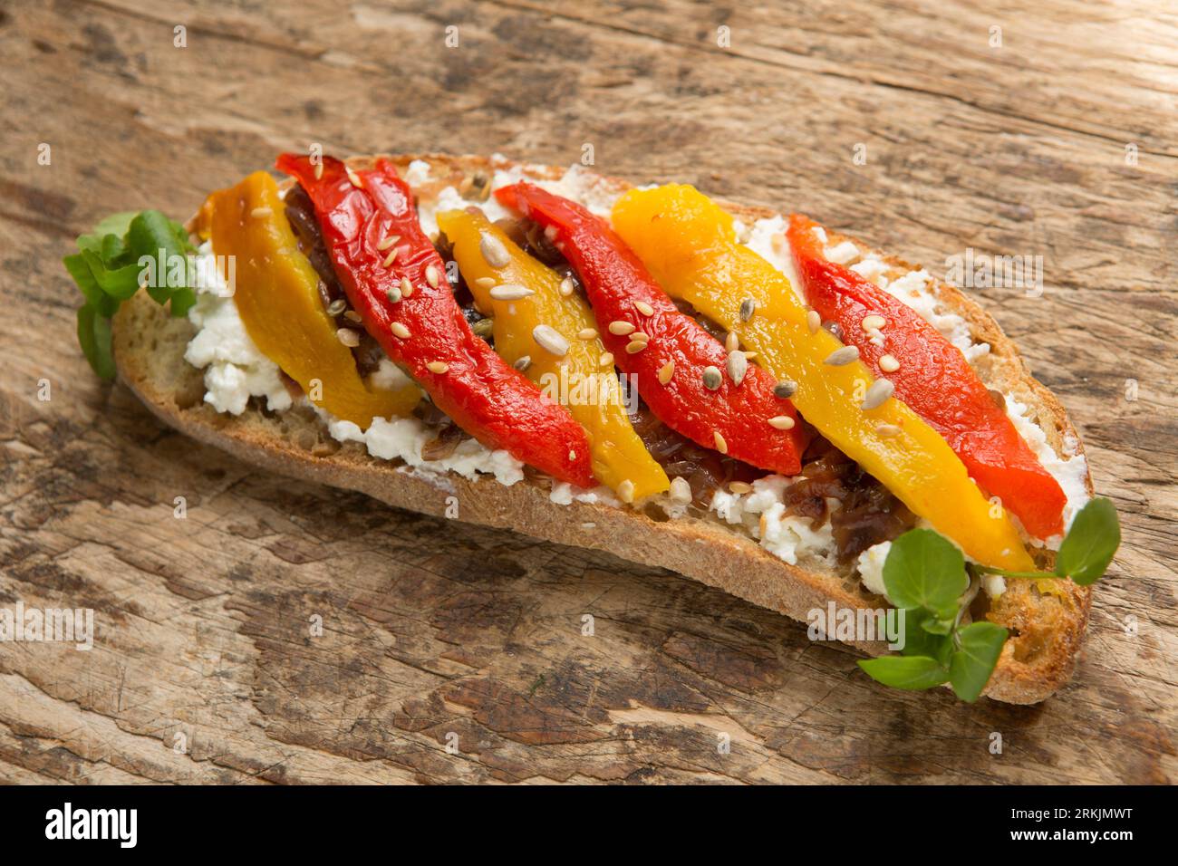 Un esempio di bruschetta fatta con pane tostato a pasta madre, ricotta, cipolle rosse caramellate e peperoni rossi e gialli grigliati e. Foto Stock