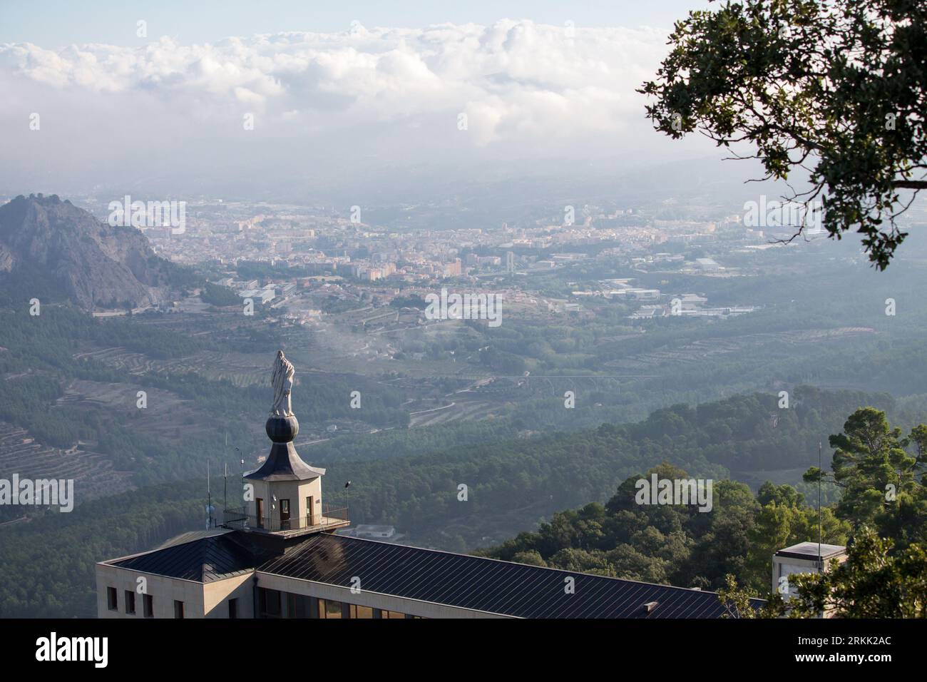 Paesaggio con le nuvole di Alcoy con il Santuario della Fontana Rossa di Alcoy in primo piano con il tetto bagnato dopo aver piovuto Foto Stock