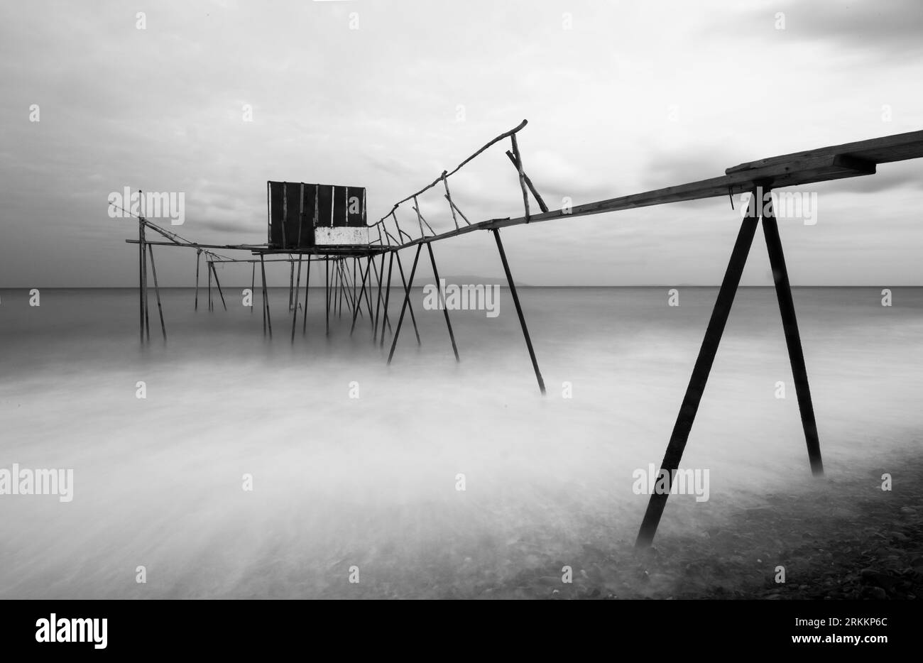 Effetto tulle a lunga esposizione in bianco e nero vicino alla costa con una piccola foto astratta del molo dei pescatori in legno Foto Stock