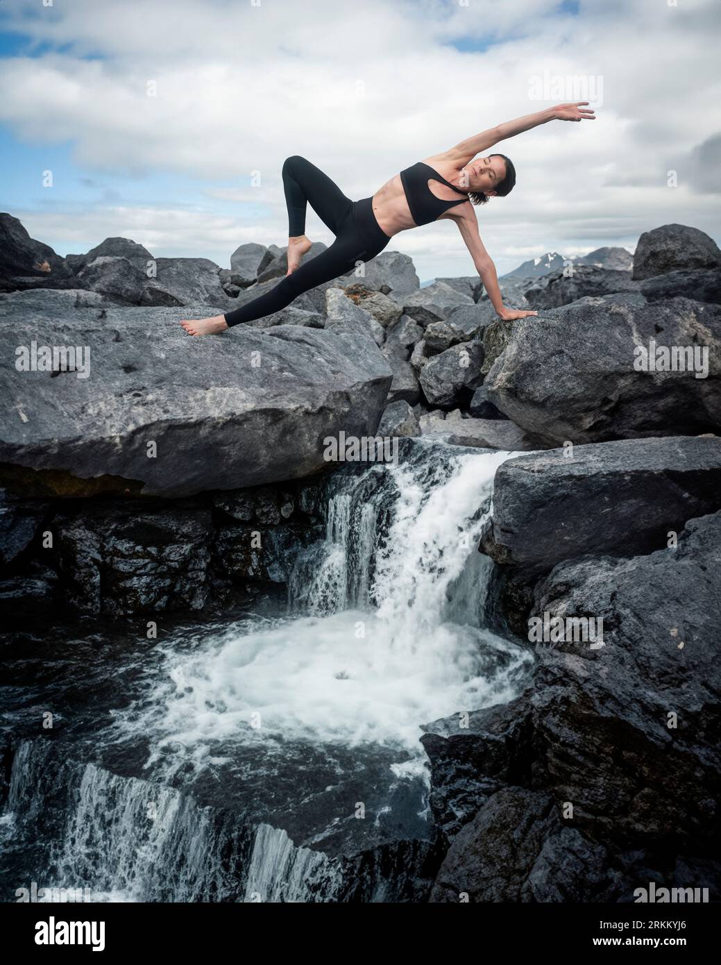 donna che pratica yoga vicino a una cascata in montagna. Foto Stock