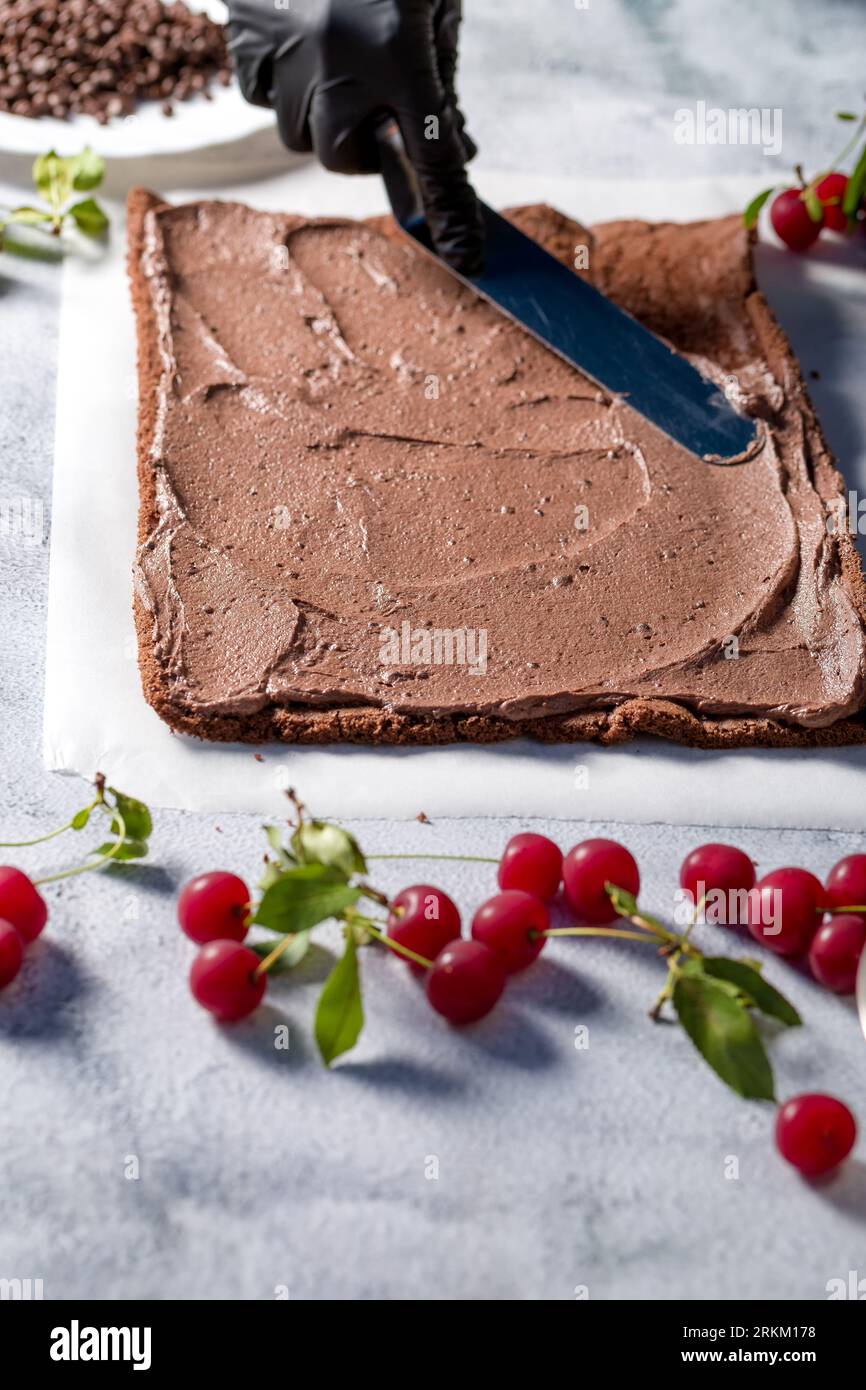 Il processo di preparazione del rotolo di cottura in cucina con ciliegie e cioccolato grattugiato. Cucina casalinga Foto Stock