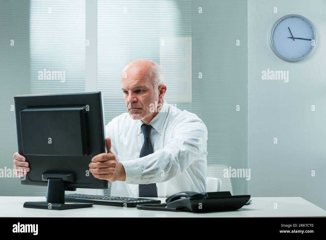 stern dirigente senior afferra lo schermo del suo computer, suggerendo problemi finanziari o errori imprevisti. Cerca di correggere rapidamente con la sua firma Foto Stock