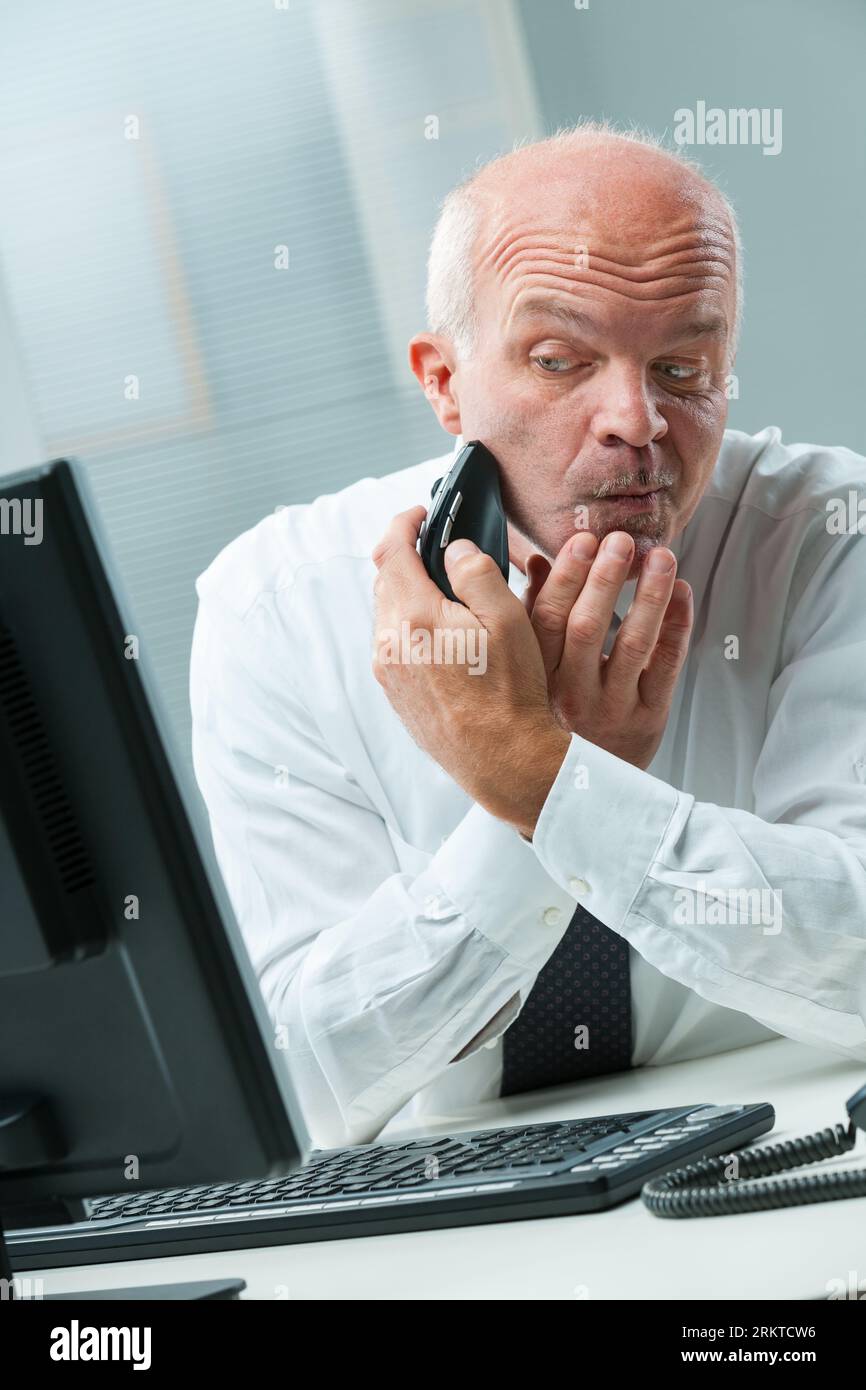 rappresentazione comica di un uomo d'affari maturo in bianco e nero che usa impropriamente gli strumenti di lavoro ma che "hackera" in modo innovativo. Finge di radersi, con un monito da tavolo Foto Stock