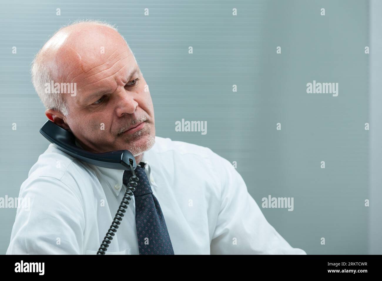 Il lavoratore di ufficio senior fatica a comprendere una telefonata, tenendo il ricevitore tra l'orecchio e la spalla. Il chiamante non è chiaro, illogico o. Foto Stock