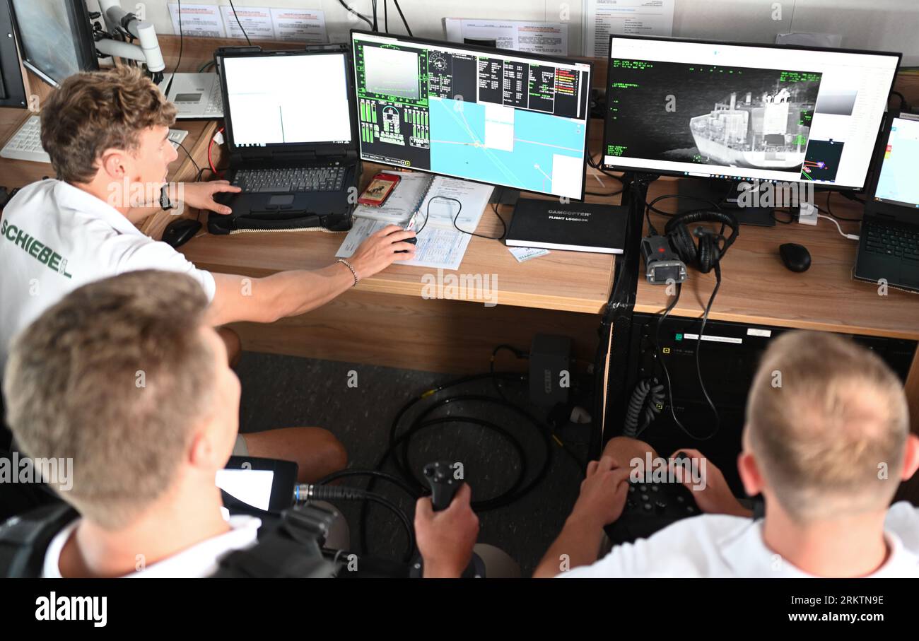 PRODUZIONE - 25 agosto 2023, bassa Sassonia, Cuxhaven: Operatore della stazione di controllo, Sébastien Thiery-Bondaneli (da sinistra a destra), operatore UAS, Aleksander Ljudivig e pilota in comando, Roman Nagy eseguono congiuntamente il volo e la misurazione con il CAMCOPTER S-100 della compagnia austriaca Schiebel. Utilizzando il drone nel Mare del Nord per cercare inquinatori, nel Mare del Nord e nel Mar Baltico si applicano limiti rigorosi per le emissioni delle navi. Il loro monitoraggio pone le autorità di fronte a sfide. Per la prima volta in Germania, un drone viene utilizzato a tale scopo in una delle rotte di navigazione più trafficate del mondo. Foto Stock