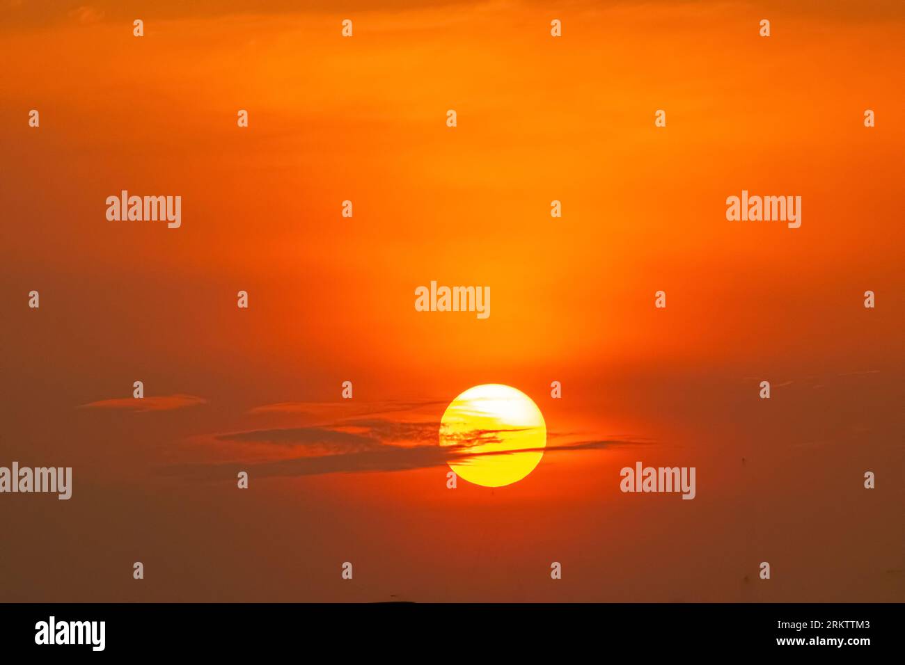 Un bellissimo teleobiettivo ravvicinato di un gigantesco disco solare giallo che tramonta attraverso un cielo arancione ardente. Foto Stock